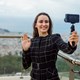 blogueira-sorridente-esta-tirando-selfie-mostrando-oi-gesto-para-sua-mini-camera-no-fundo-da-vista-da-cidade